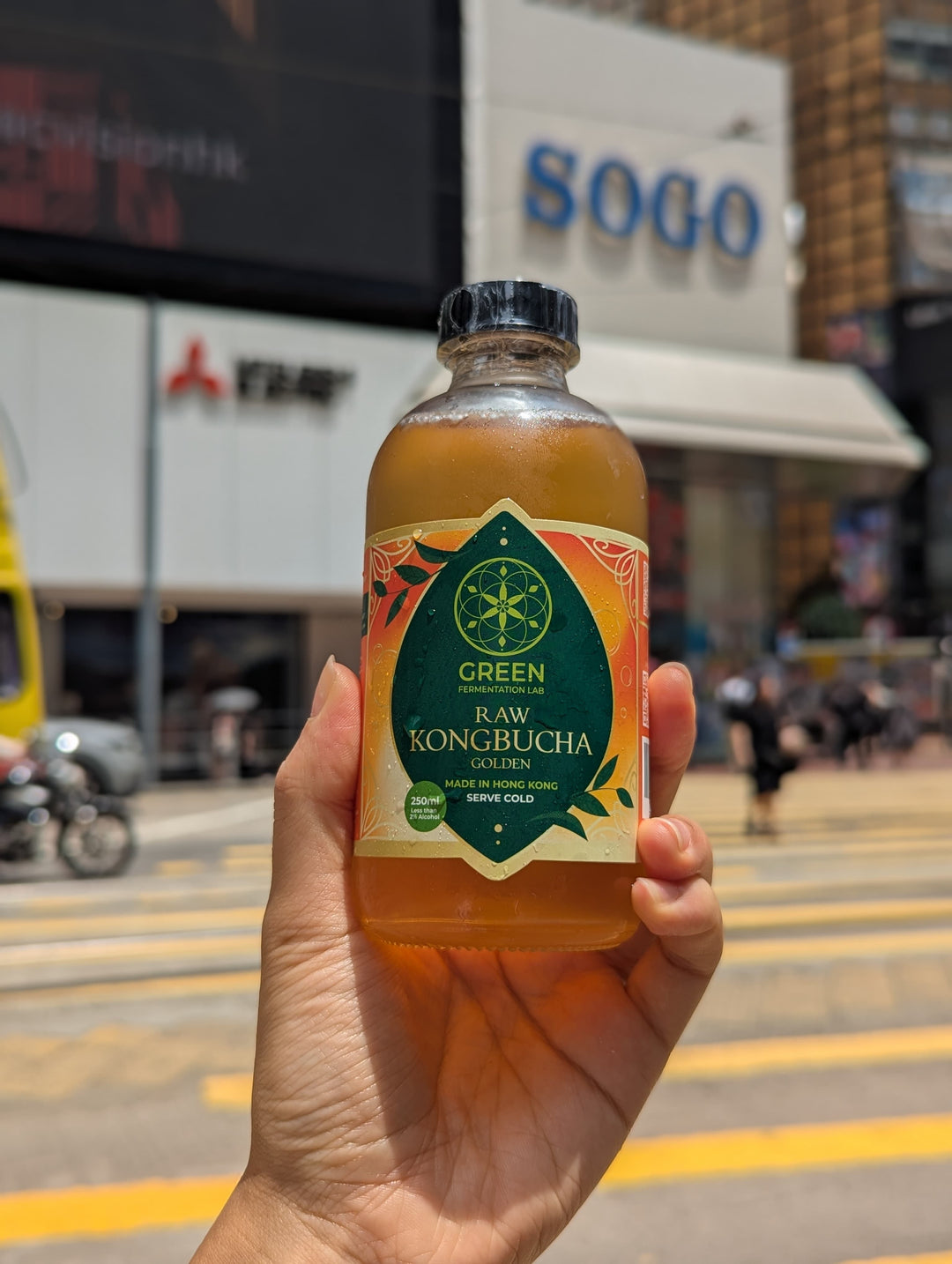 Hand holding up a bottle of kombucha against a hong kong backdrop